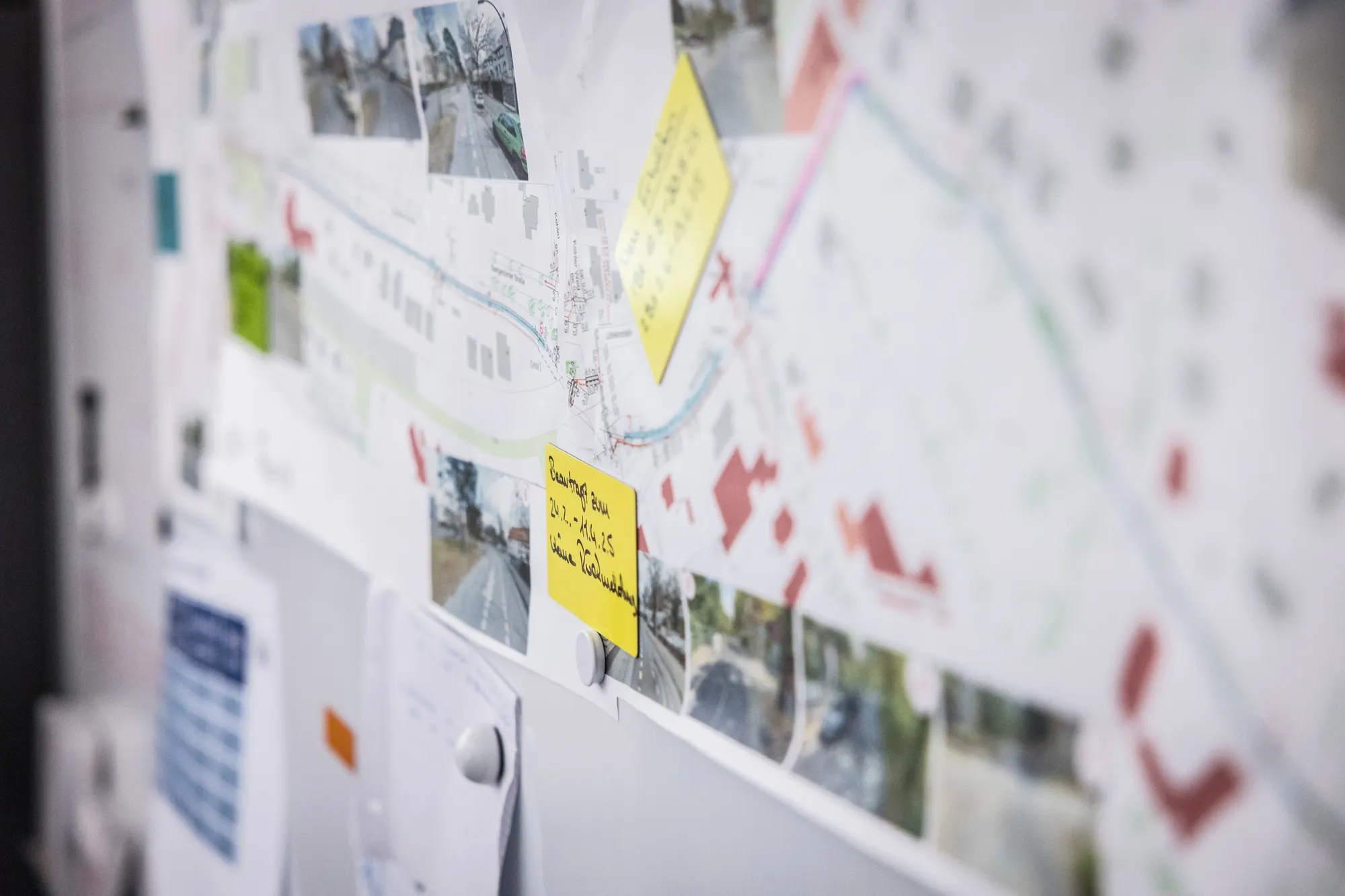 Planungswand im HAN-Büro mit Lageplan, Baustellenfotos und Notizzetteln
