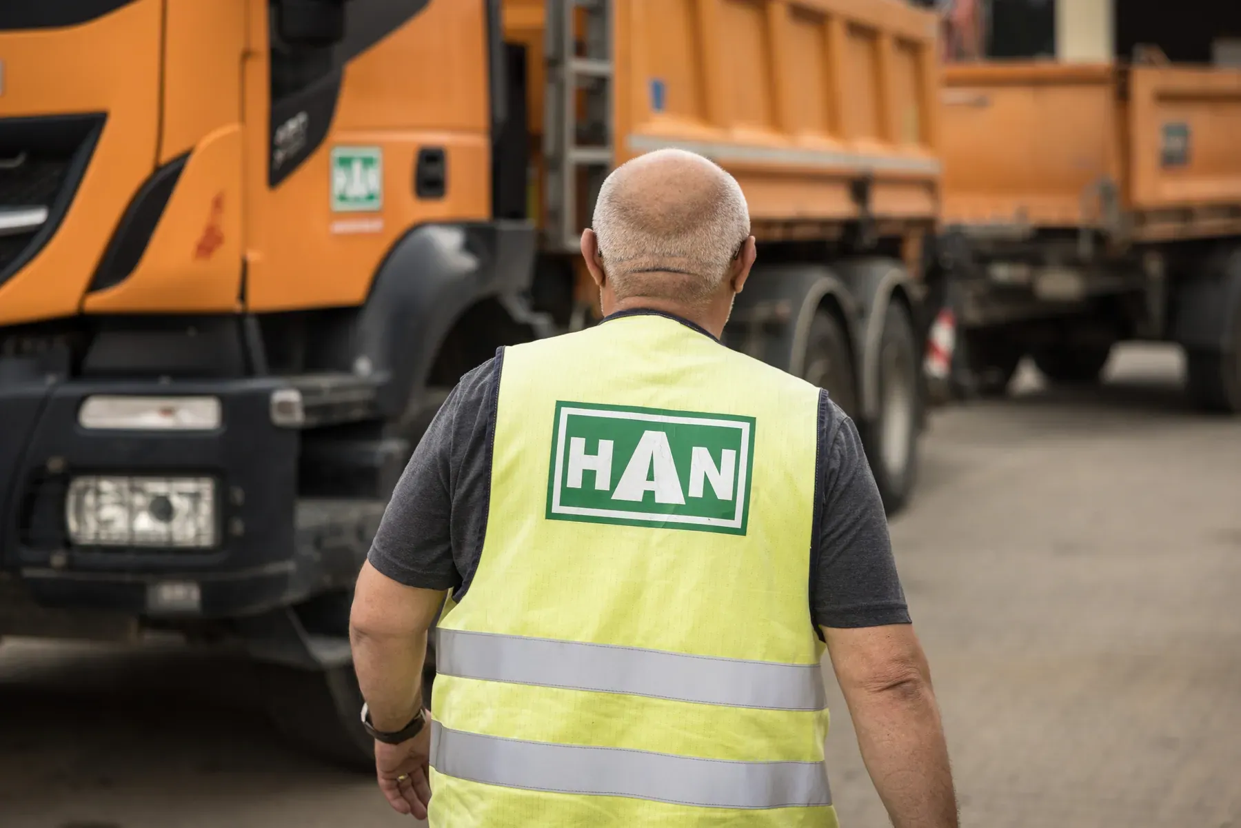 HAN-Mitarbeiter in Warnweste geht zu einem orangen HAN-Kipper-Lkw