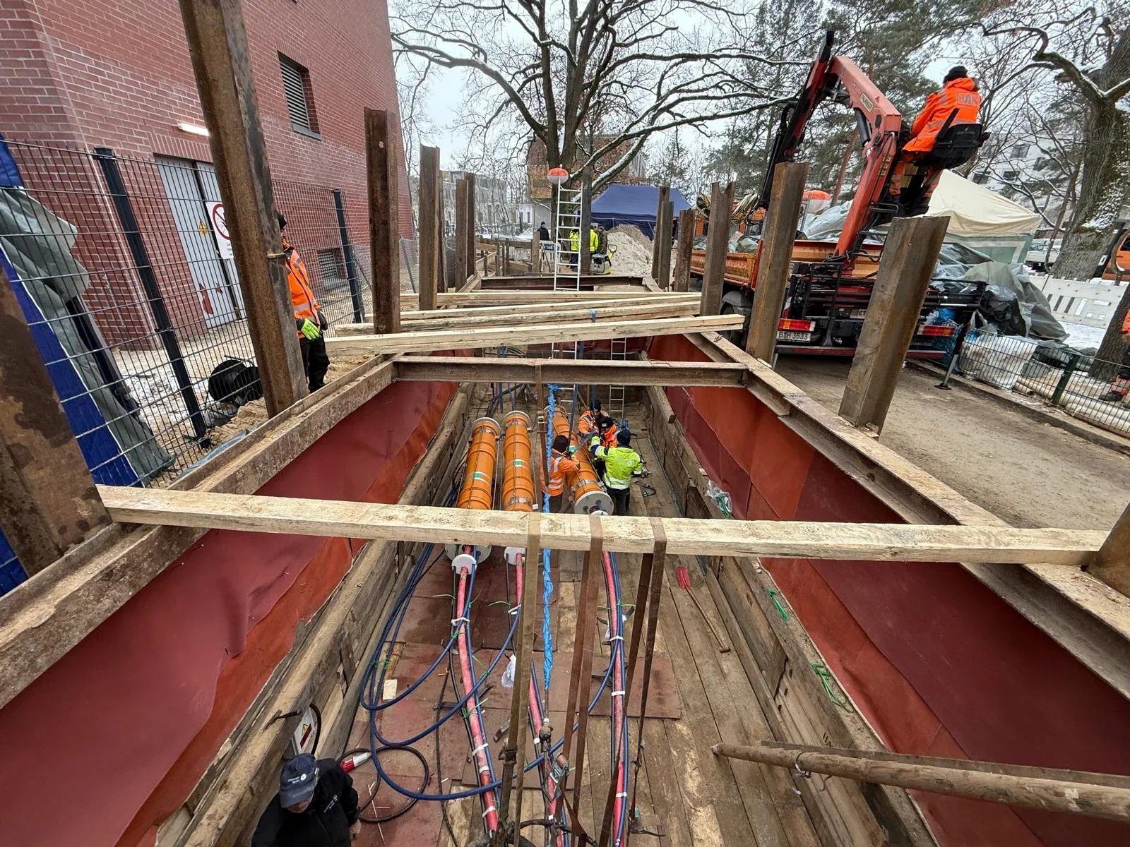 HAN-Baustelle in Berlin: verbauter Graben mit Kabelschutzrohren, Ladekran und Kolonne im Einsatz