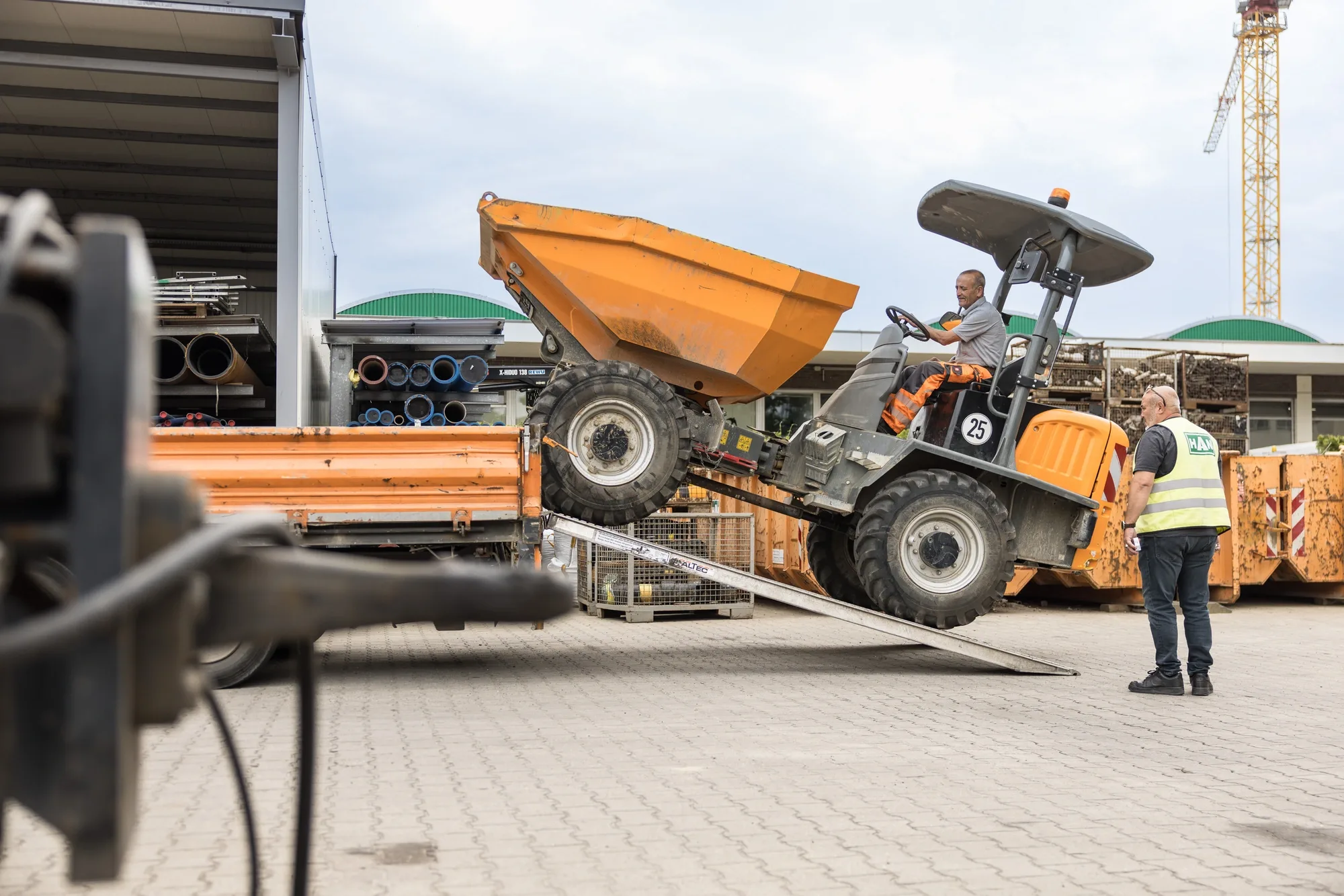 HAN-Betriebshof: ein Dumper fährt von einem Transporter, ein Mitarbeiter weist ein